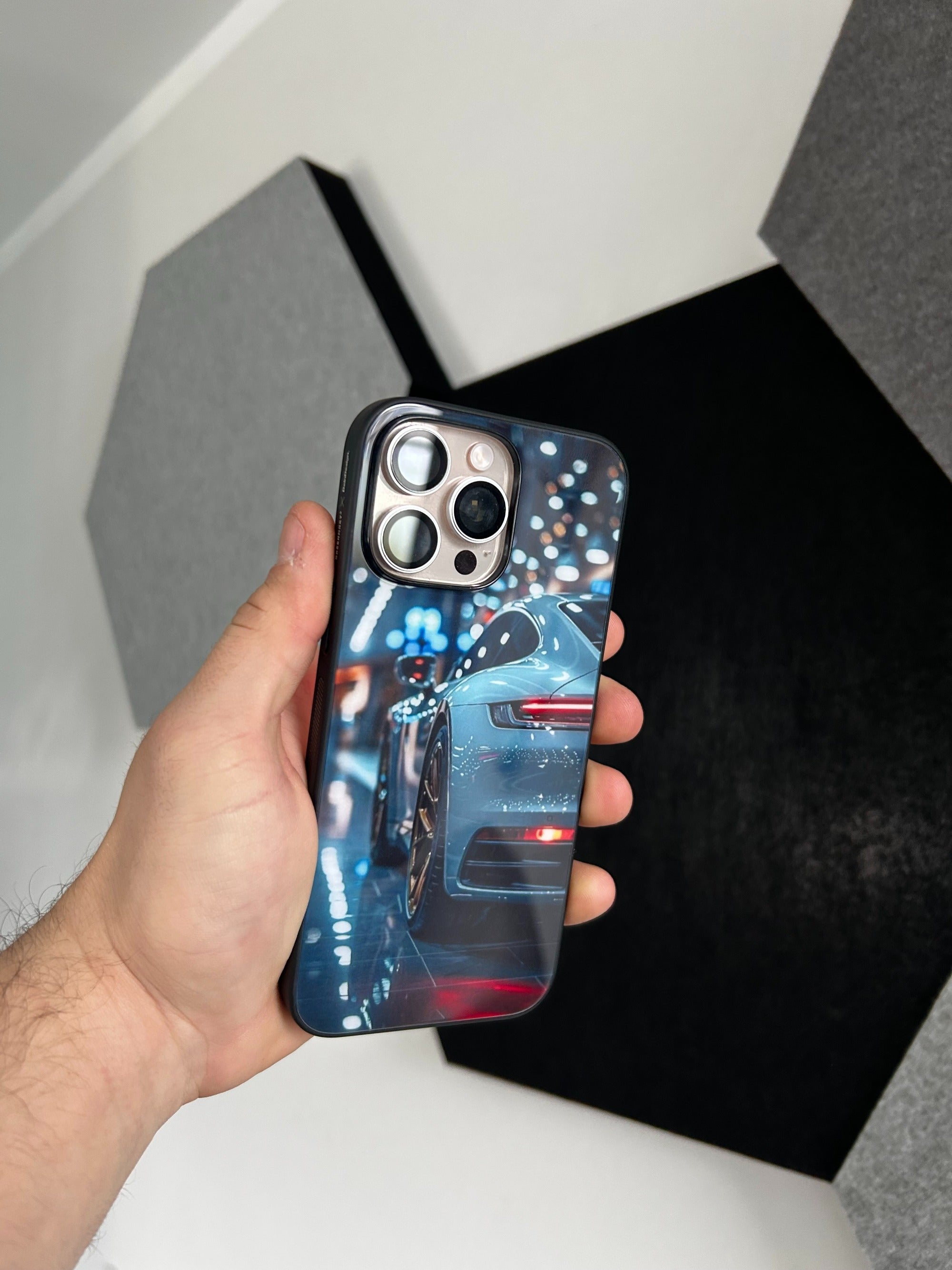 Hand hält eine personalisierte GREENMNKY Handyhülle mit Auto Motiv und Dreifachkamera Ausschnitt, Nahaufnahme vor dunkler Wand im Hintergrund