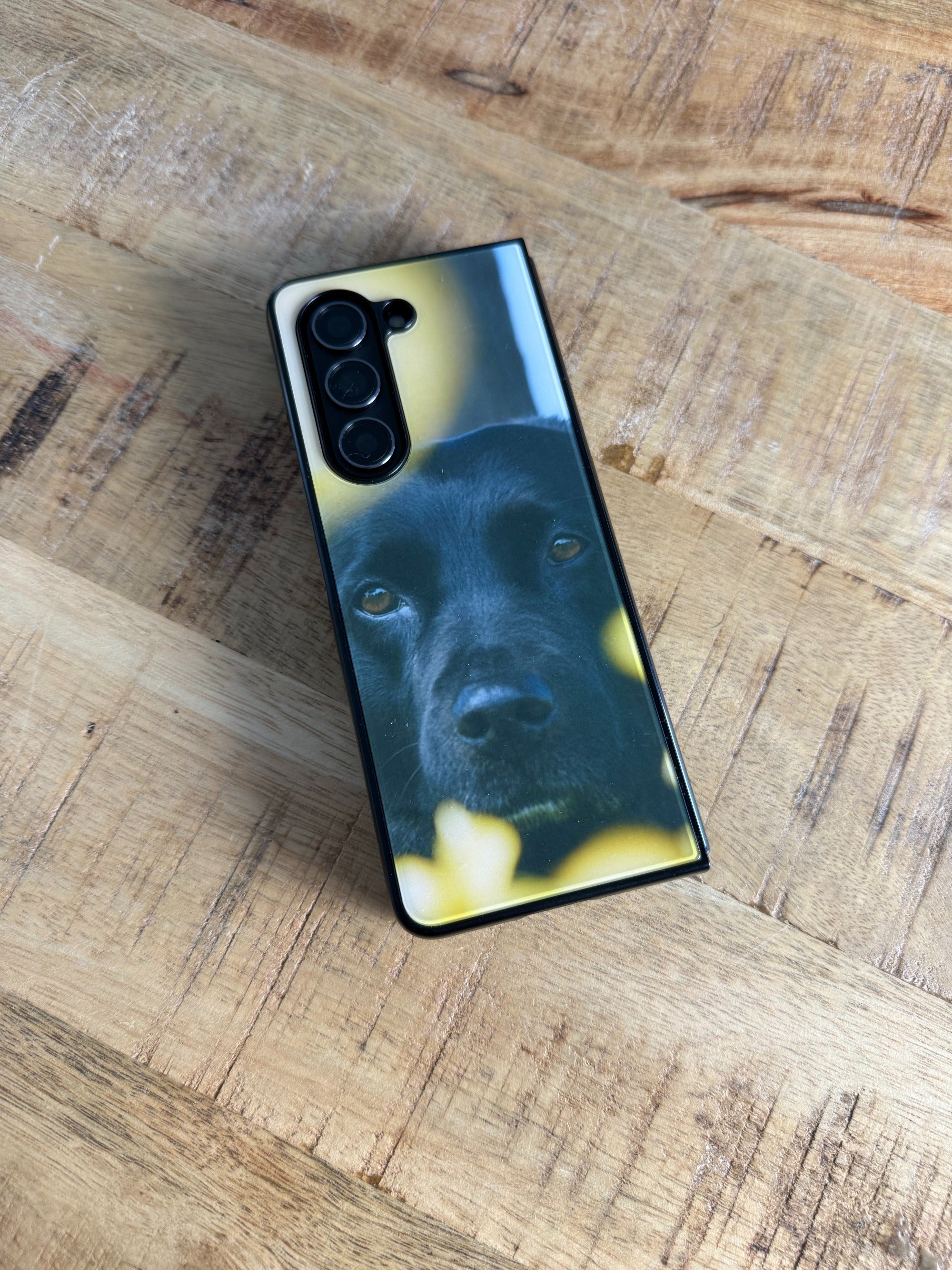 Personalisierte GREENMNKY Samsung Handyhülle mit Hunde Portrait Motiv liegt auf einem Holztisch, Rückseite mit Mehrfachkamera Ausschnitt sichtbar