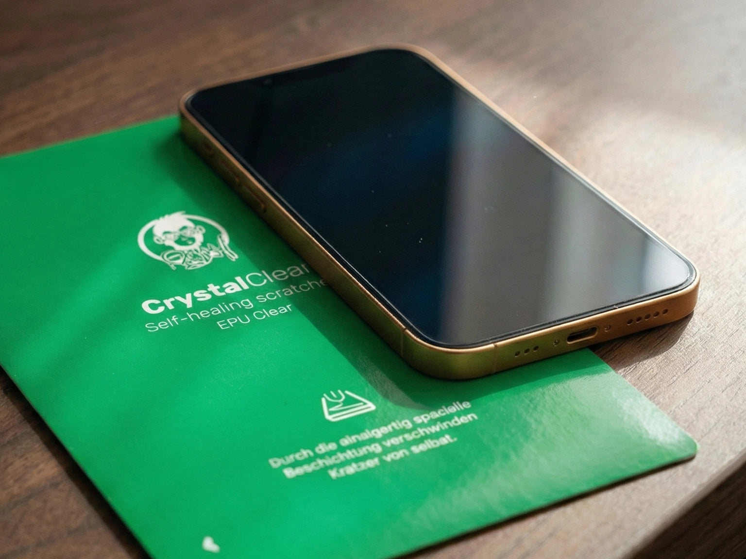 Smartphone liegt auf einer grünen GREENMNKY CrystalClear Unterlage auf einem Holztisch, das Display wirkt glatt und klar als Vergleich zur dünnen Panzerfolie